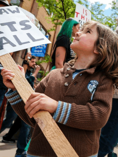 "This Law Hurts" sign held by a child