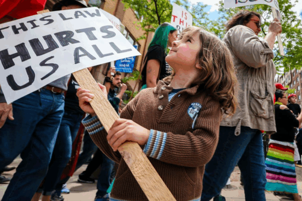 "This Law Hurts" sign held by a child