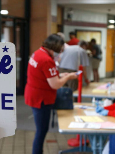 Image of a polling place with two people and a sign that reads, "vote here"