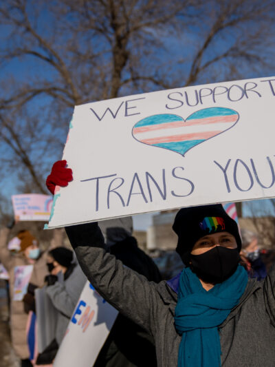 Person with a sign that reads "we support trans youth"
