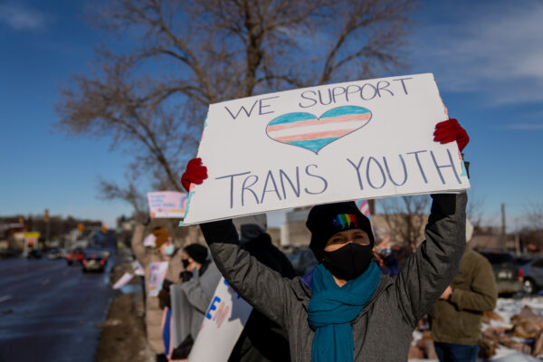 Person with a sign that reads "we support trans youth"
