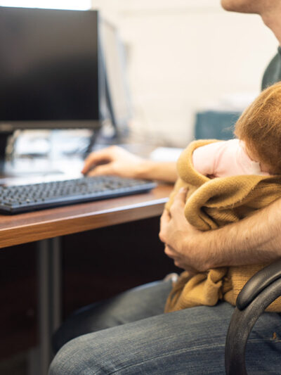 A man holding a baby while on a computer.