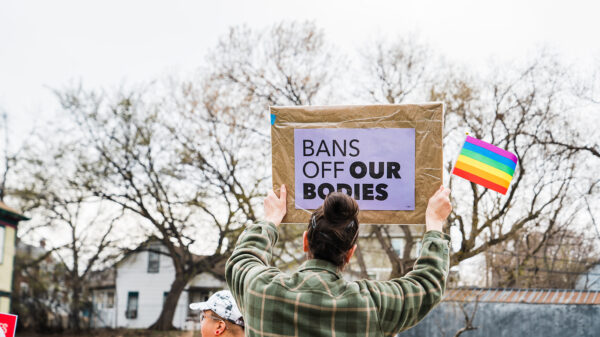 person holding a bans off our bodies sign with a rainbow flag