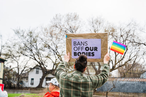 person holding a bans off our bodies sign with a rainbow flag