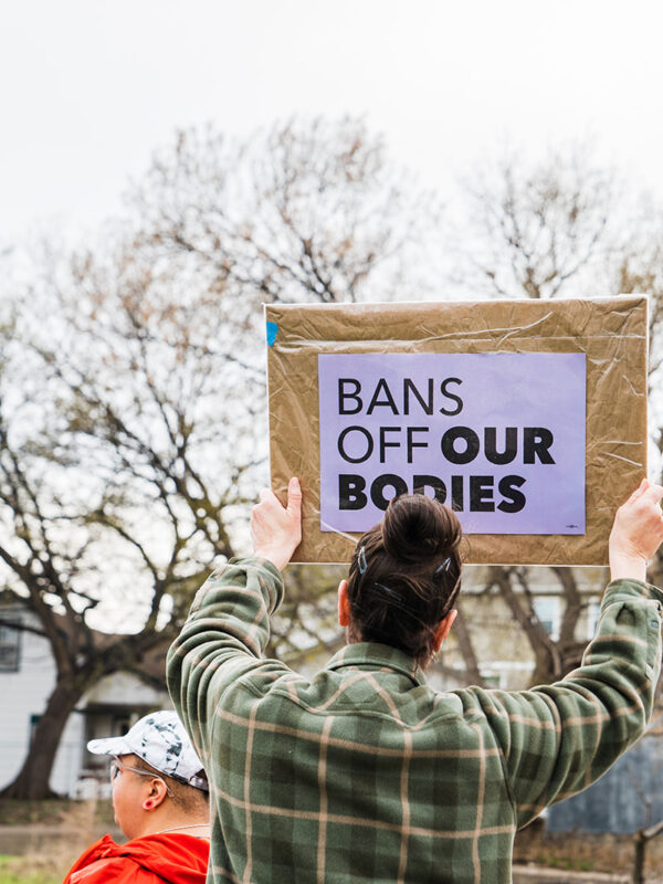 person holding a bans off our bodies sign with a rainbow flag