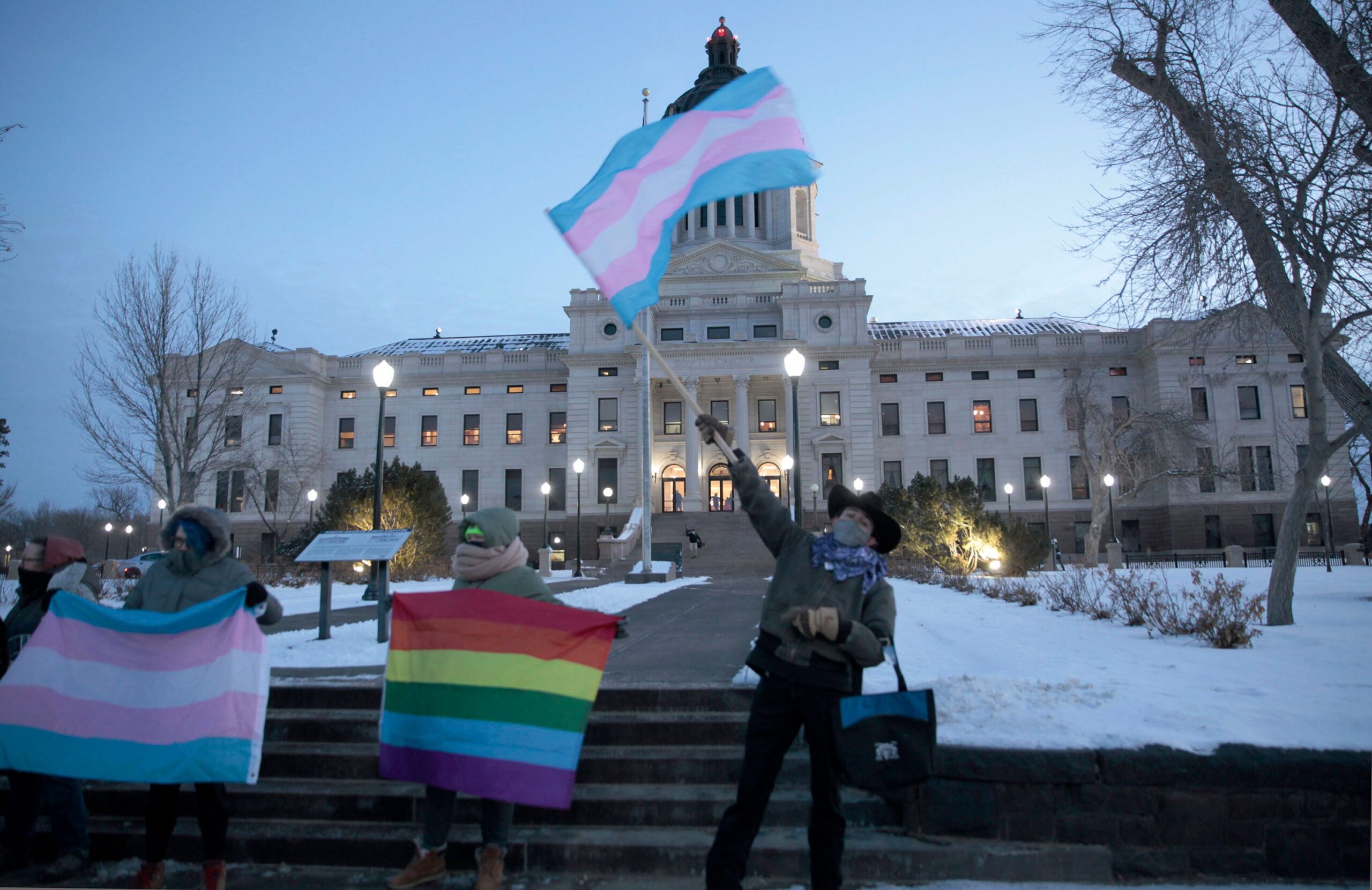 Person holding a trans flag in front of the South Dakota state capitol