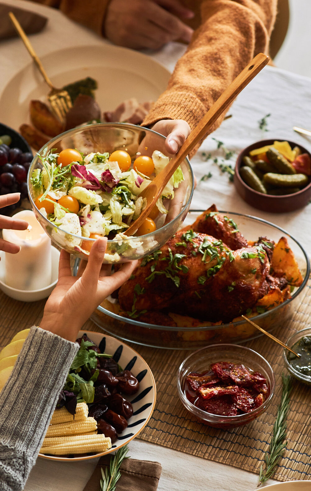 A multi-ethnic group of people sharing a festive, communal meal at a dining table with roasted chicken, salad, bread, fruit, and wine.