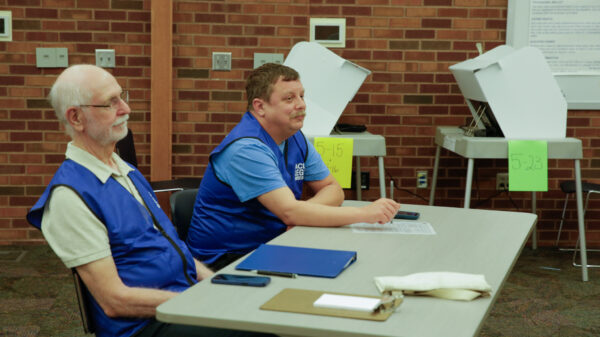 Two men sitting at a table at a polling location wearing blue ACLU legal observer vests