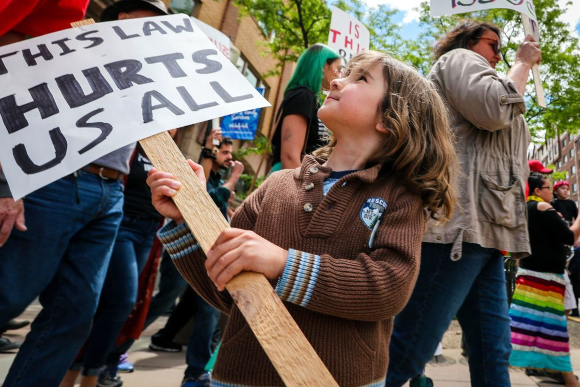"This Law Hurts" sign held by a child 