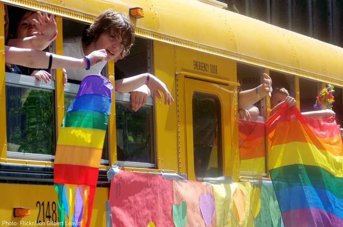 Students on a school bus waving LGBT flags