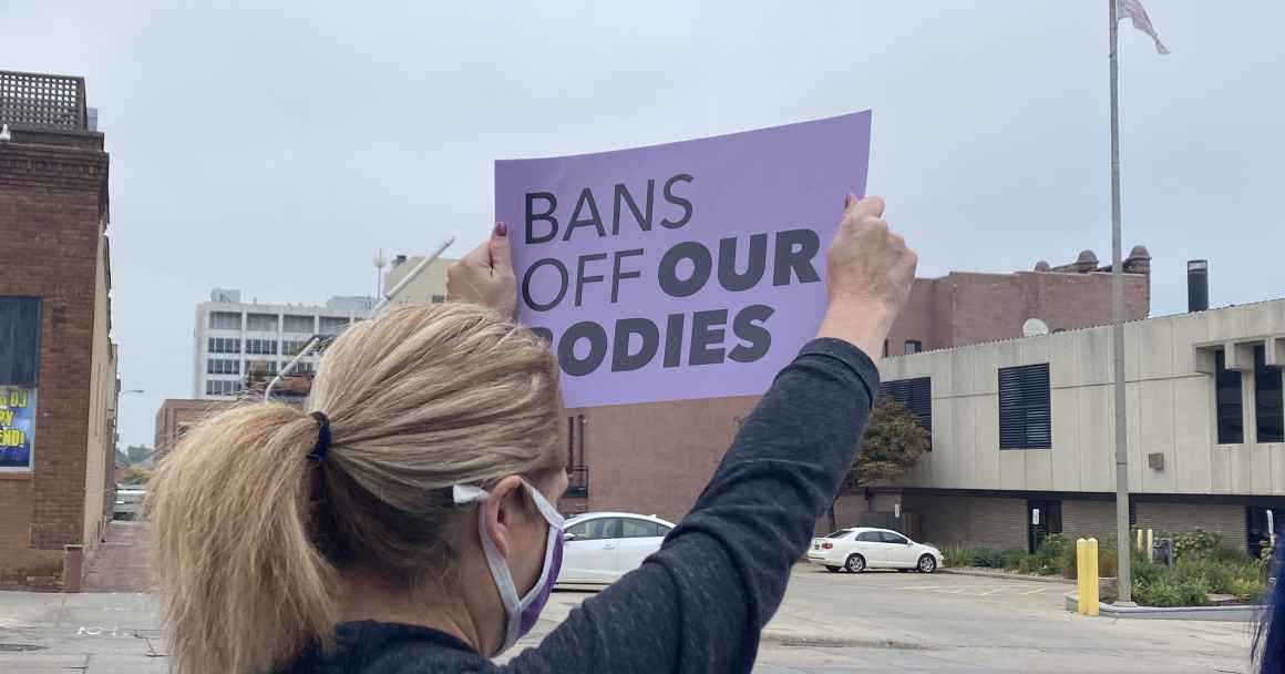 Image of a person holding a sign that reads, "BANS OFF OUR BODIES."