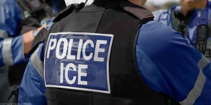 Close-up of POLICE ICE marking on the back of a stab proof vest uniform worn by a police officer.