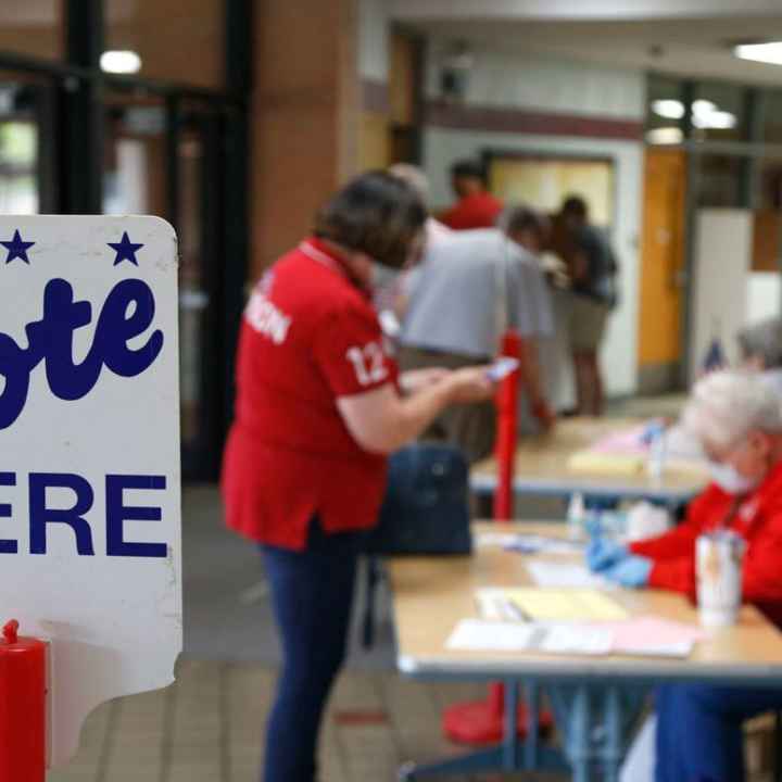 Image of a polling place with two people and a sign that reads, "vote here" 