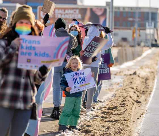 Image of a kid holding a sign that says, "Let trans kids play"